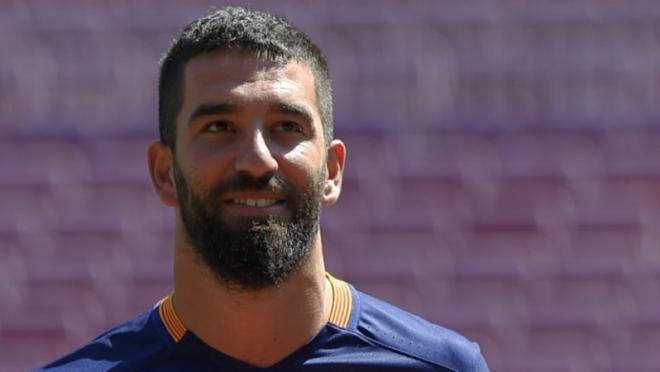 Arda Turan biting his bottom lip in a smile and looking up an away. 